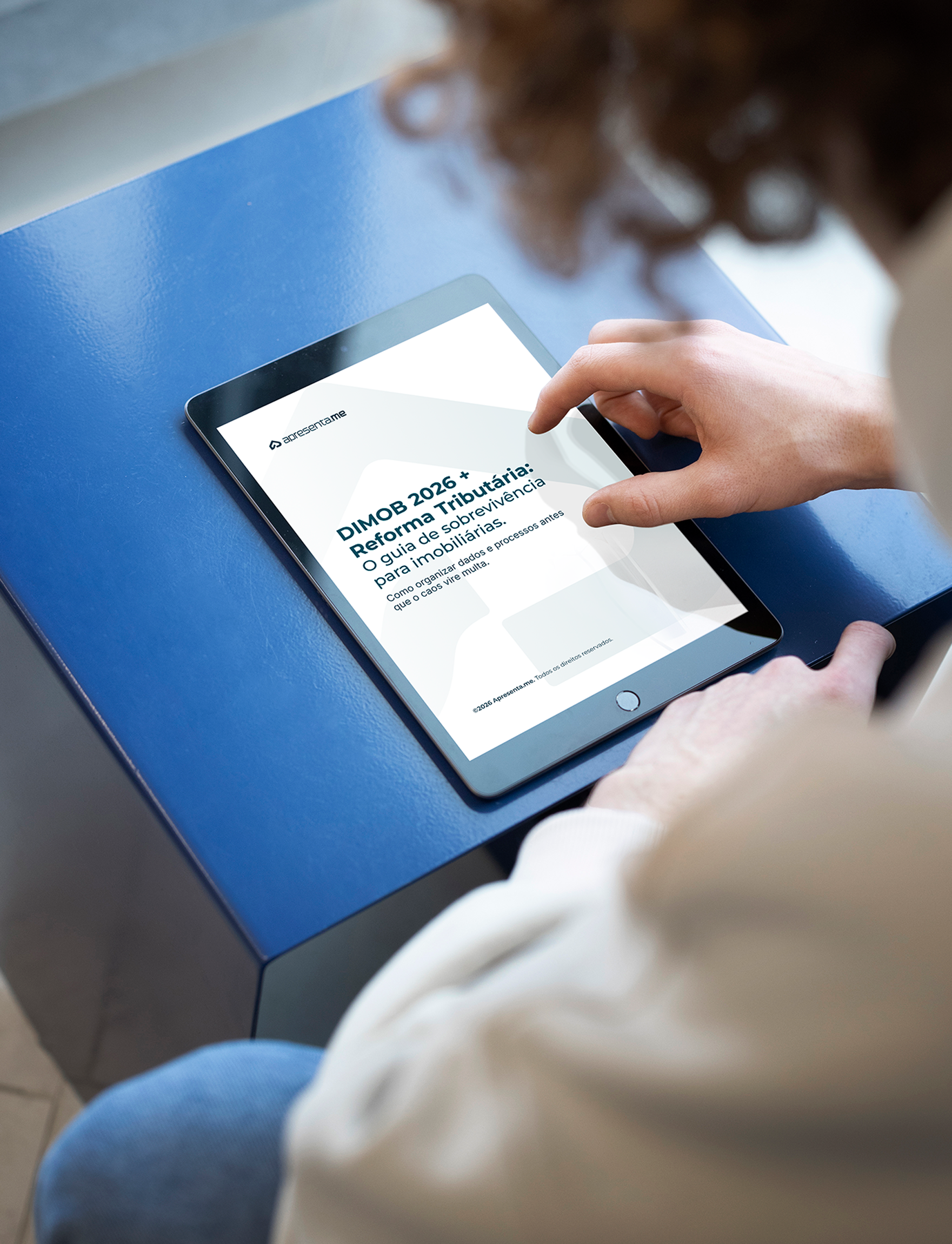 Pessoa segurando um tablet com a capa do e-book DIMOB 2026 + Reforma Tributária na tela